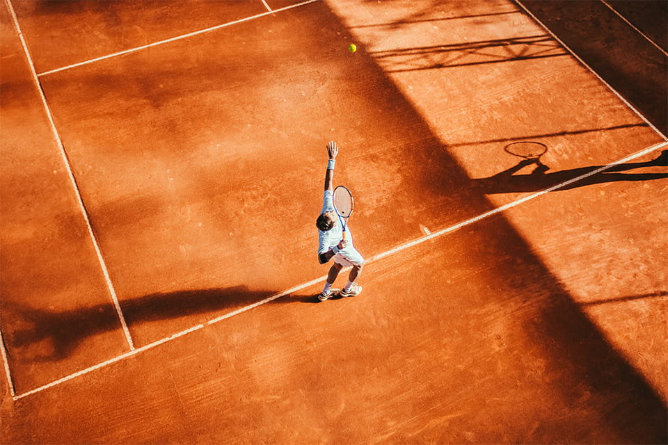 Теннисист делает подачу на оранжевом корте