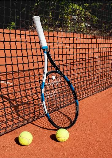 Теннисная ракетка и два теннисных мяча стоят у сетки корта